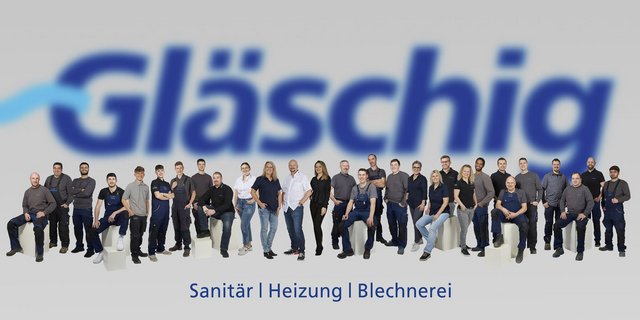 Eine Gruppe von Mitarbeitern steht zusammen, lächelnd, in Arbeitskleidung, vor einem verschwommenen Logo im Hintergrund.