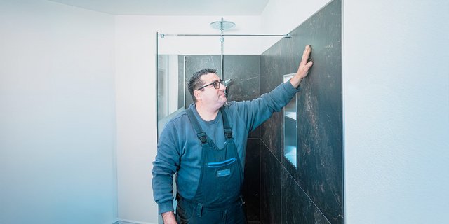 Ein Handwerker inspiziert sorgfältig die Wandfliesen in einem modernen Badezimmer mit hellem, minimalistischen Design.