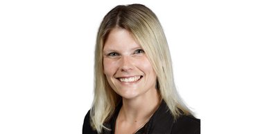 Eine lächelnde Frau mit blonden Haaren trägt ein schwarzes Oberteil und schaut direkt in die Kamera.