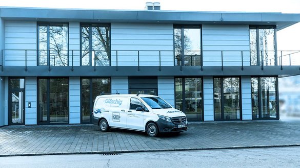 Ein modernes Gebäude mit großen Fenstern und einem Balkon, vor dem ein weißer Lieferwagen parkt.