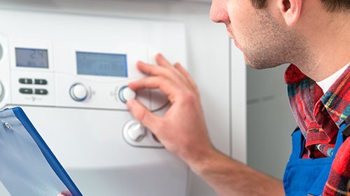 Ein Anlagenmechaniker mit einem Klemmbrett dreht an einer Heizungsanlage