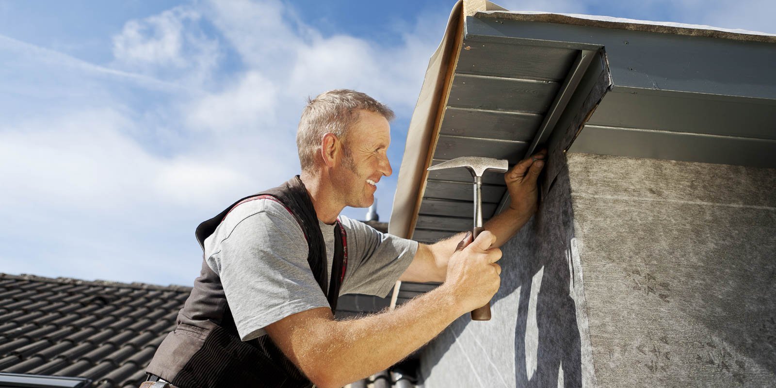 Ein Dachdecker der an einem Dach arbeitet und einen Hammer in der Hand hat