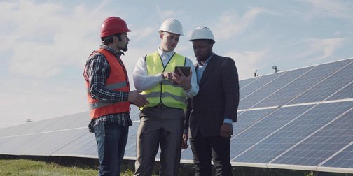 Eine Photovoltaikanlage auf einer Wiese mit drei Männern die auf ein Tablet schauen