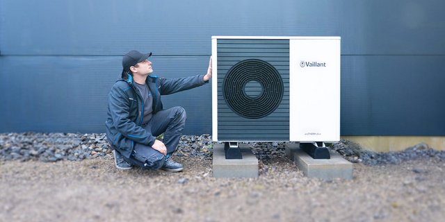 Ein Techniker kniet neben einer modernen Wärmepumpe von Vaillant, während er sie aufmerksam betrachtet.